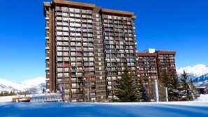 A multi-story hotel with balconies, located near a body of water and mountains.