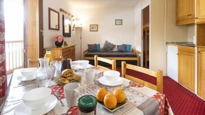 A dining area with a table set for breakfast, a sofa in the background, and wooden cabinets. - Roche Blanche 83 by Interhome (Val Thorens)