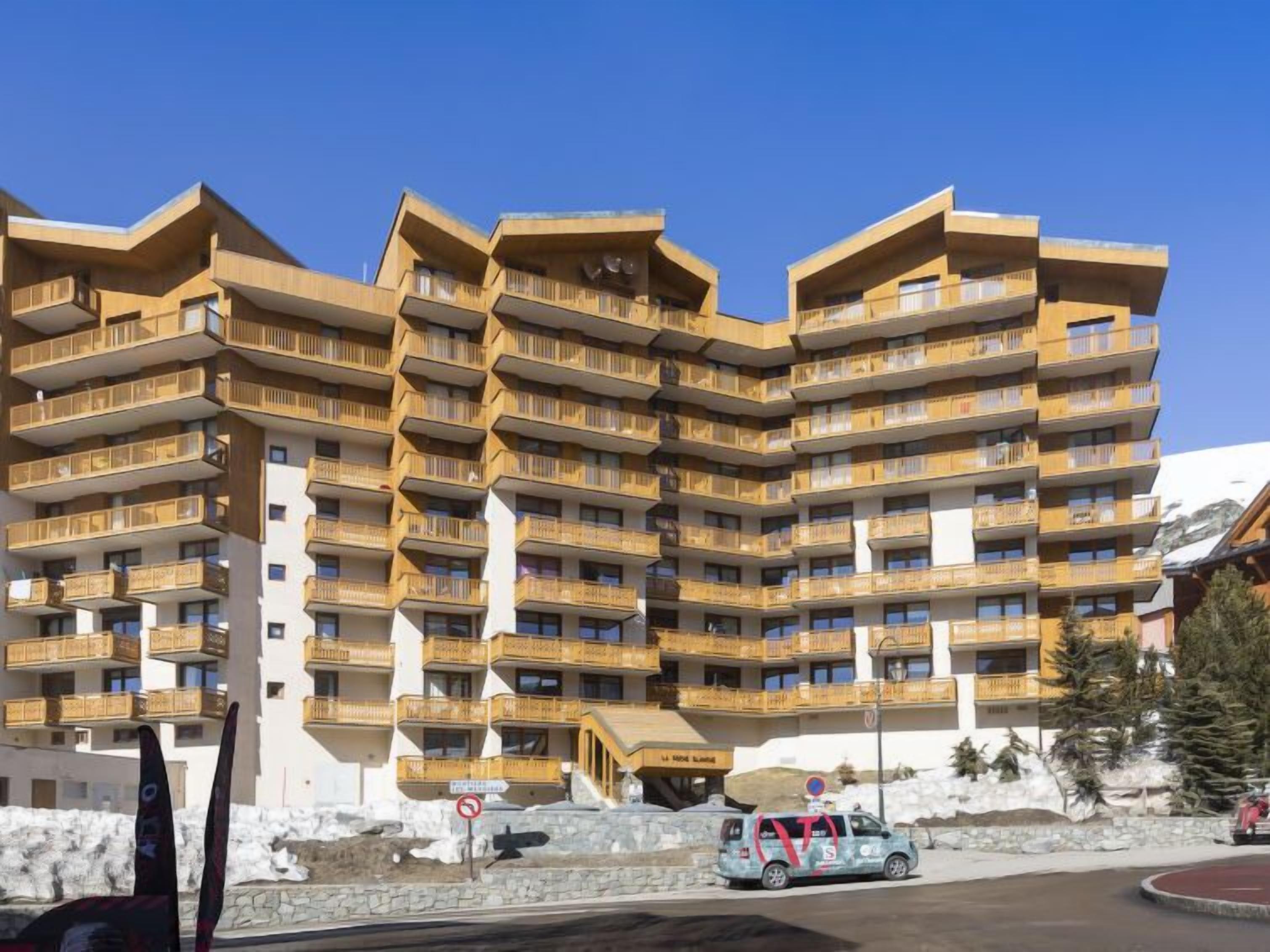 A multi-story hotel with balconies, a ski lift, and a mountainous backdrop.