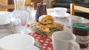 A dining table set with white plates, cups, and a glass pitcher. There is a basket of pastries and a jar of jam on the table. - Roche Blanche 83 by Interhome (Val Thorens)