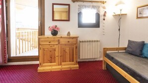 A room with a wooden dresser, a bed with a grey mattress, a red carpet, a radiator, a window with a view, and a wall-mounted mirror. - Roche Blanche 83 by Interhome (Val Thorens)
