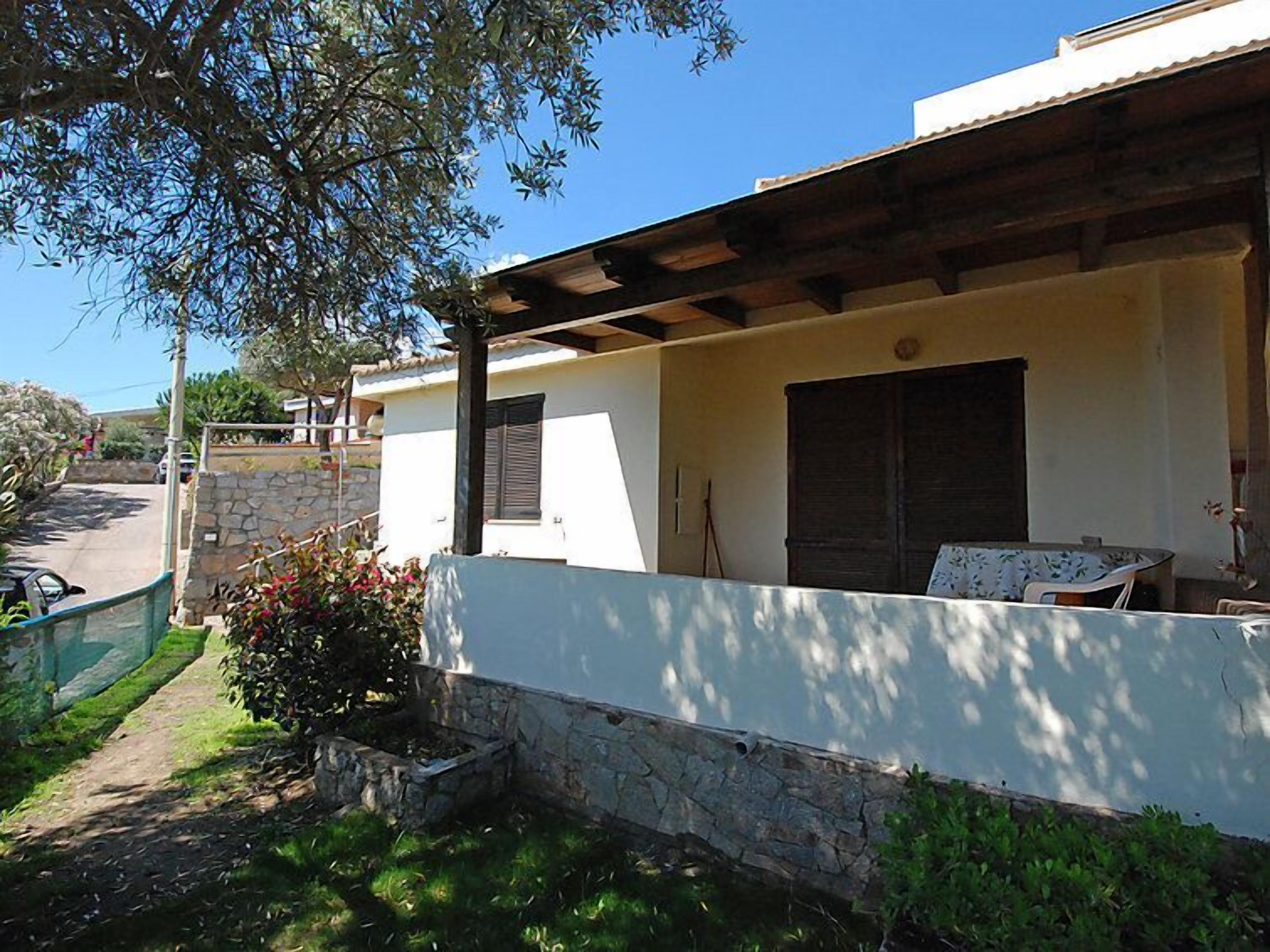 Un espace extérieur aménagé avec des places assises, protégé par un toit, doté de murs en pierre et d’une pergola.
