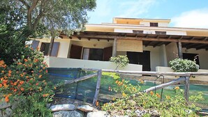 A building with a flat roof, a balcony, and a stone wall in the foreground. - Belvedere Bilo by Interhome (Costa Rei)