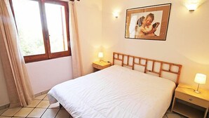 A bedroom with a large bed, two bedside tables with lamps, a window with curtains, and a framed picture on the wall. - Belvedere Bilo by Interhome (Costa Rei)