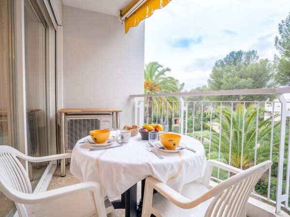 Varanda com mesa posta para dois, incluindo toalha branca, duas cadeiras brancas e um guarda-sol amarelo.