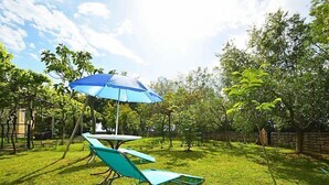 Un cortile con un ombrello blu, due poltrone verdi e un tavolino.