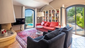 Uma sala de estar com um sofá vermelho, poltronas pretas, uma estante de livros e uma televisão.