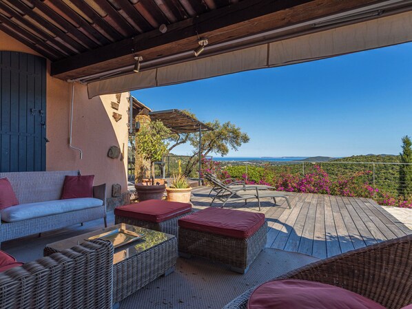 An outdoor patio with wicker furniture, a covered seating area, and a view of the landscape.