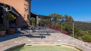 Uma área de piscina com espreguiçadeiras, um deck de pedra e vista para a paisagem ao redor.