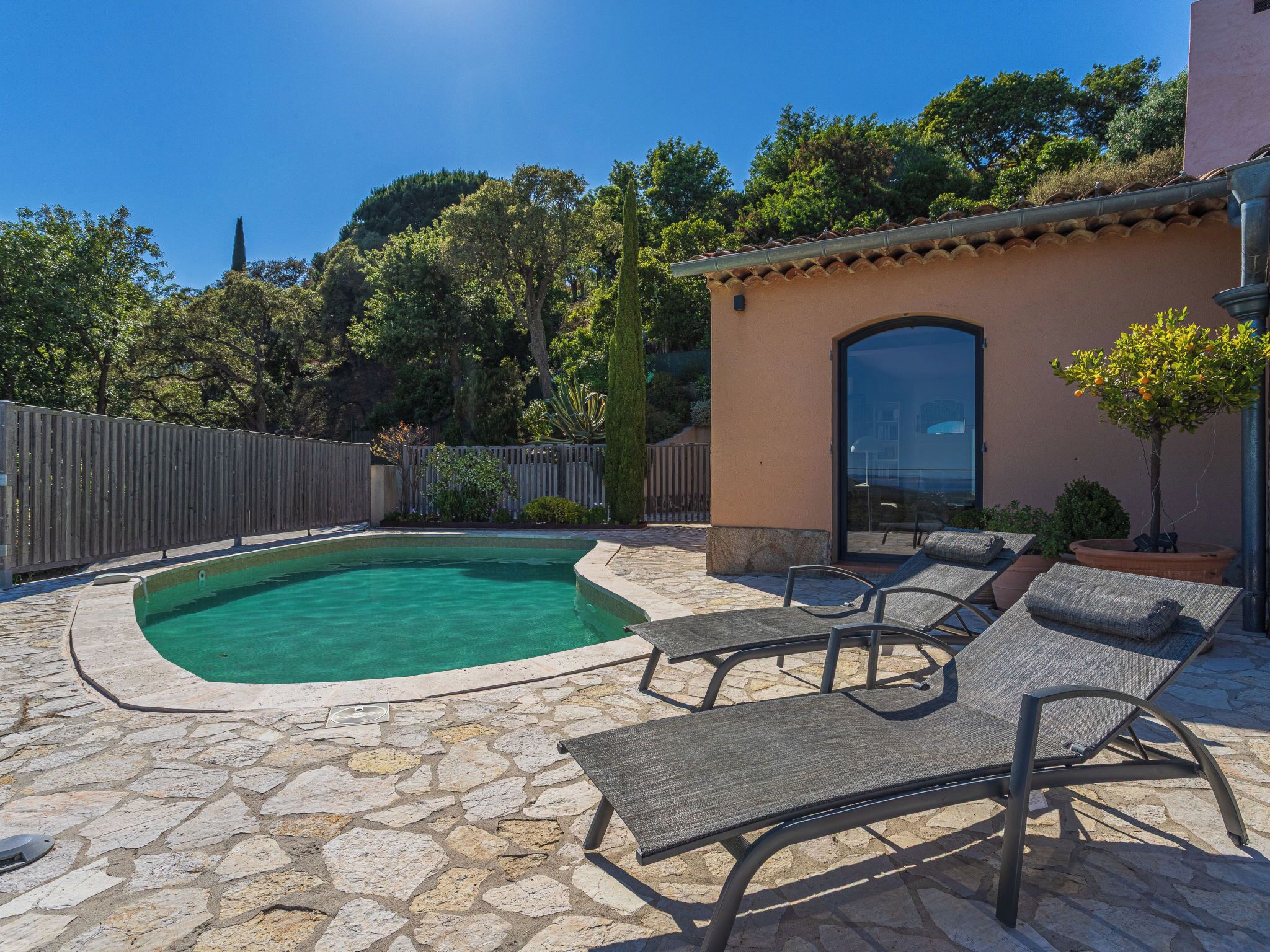 Una piscina con sillas de descanso, un patio de piedra y una cerca de madera.