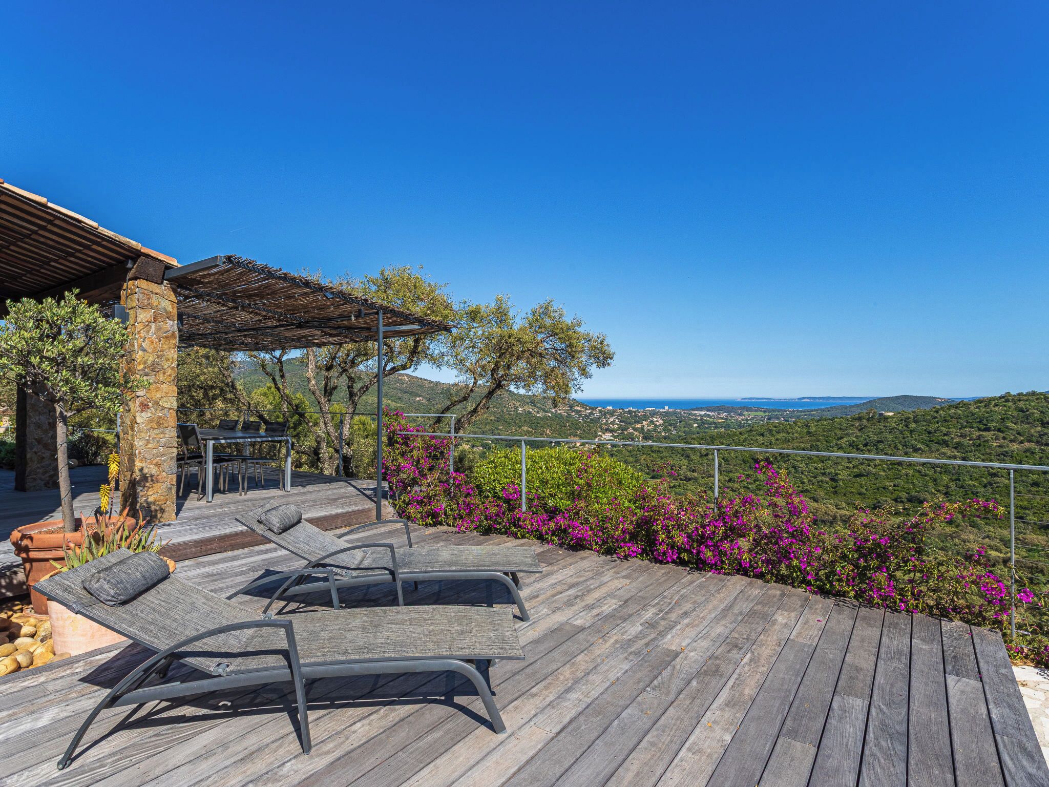 A wooden deck with lounge chairs, a stone pillar, and a pergola.
