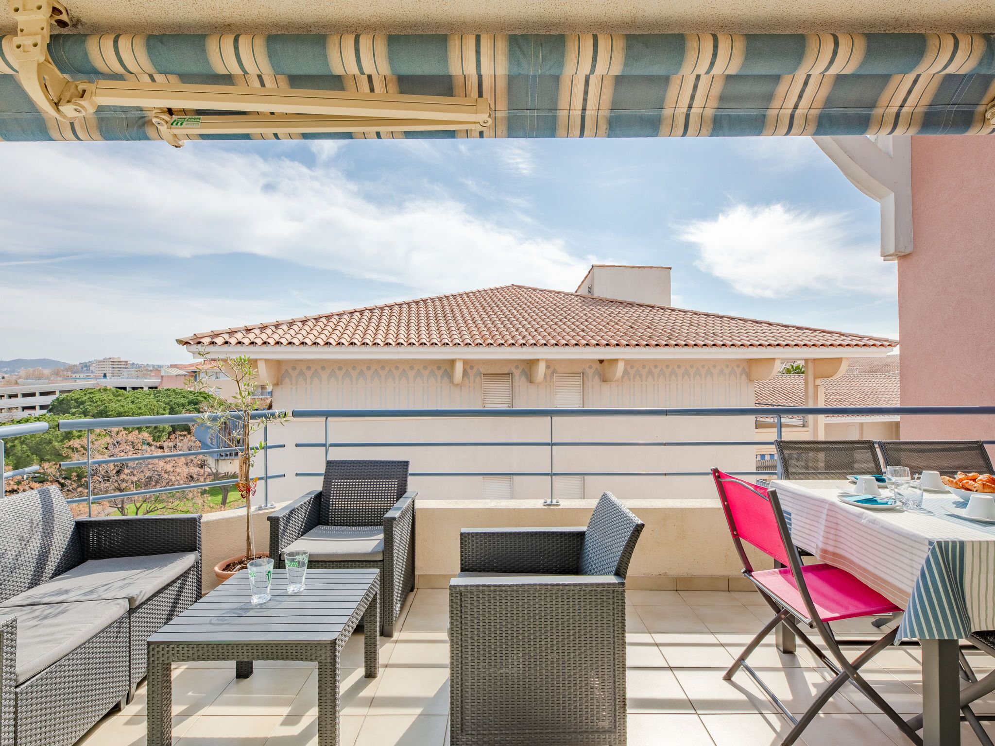 Eine Außenpatio-Terrasse mit Korbmöbeln, einem Esstisch und Blick auf ein Gebäude mit einem Ziegeldach.
