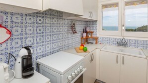 Une cuisine avec des meubles blancs, une cuisinière, une machine à café et une fenêtre donnant sur la mer.
