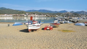 Une plage où plusieurs petits bateaux sont amarrés sur le sable, une étendue d’eau calme et, au loin, une ville entourée de montagnes.