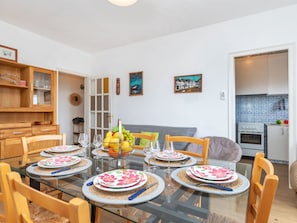 A dining area with a glass table set for six, surrounded by wooden chairs.