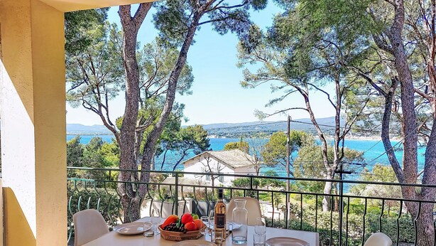 Une table dressée pour deux personnes, avec vue sur la mer et les arbres.