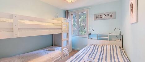 A bedroom with bunk beds, a bedside table, a window with a view, and a wall-mounted shelf.