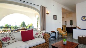 Ein gemütlicher Wohnbereich mit einem Rattan-Sofa, einem kleinen Tisch und Blick ins Freie.