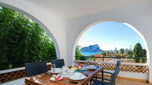 Ein Esstisch mit Stühlen, Blick auf das Meer und ein Berg im Hintergrund.