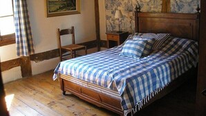 Une chambre à coucher avec un lit en bois, une literie à carreaux, une chaise, une table de chevet, une lampe et un tableau accroché au mur.