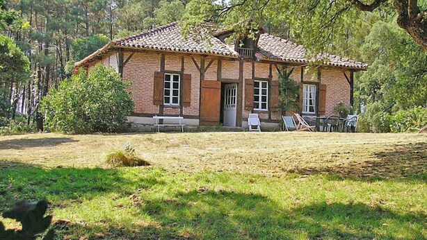 Une maison de campagne au toit recouvert de tuiles, aux murs en briques et dotée d’une cour verdoyante aménagée avec du mobilier d’extérieur.
