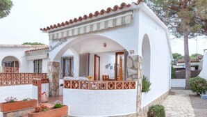 Un bâtiment blanc agrémenté de détails en pierre et surmonté d’un toit en tuiles. On y trouve des espaces extérieurs aménagés avec des chaises et des tables, ainsi qu’un petit jardin avec des plantes en pot.
