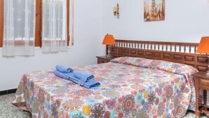 Une chambre à coucher avec un lit, deux lampes de chevet, une fenêtre avec des rideaux et un tableau accroché au mur.