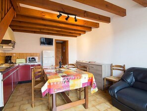A cozy kitchen with wooden beams, a dining table set with a colorful tablecloth, and a black leather couch.