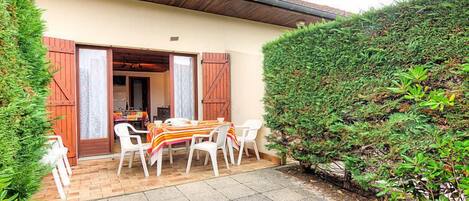 Un patio con mesa y sillas, una puerta de madera y un seto.