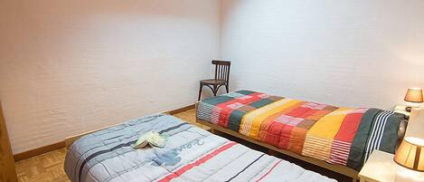 Un dormitorio pequeño y acogedor con dos camas, un tragaluz, una silla y una mesita de noche con lámpara.