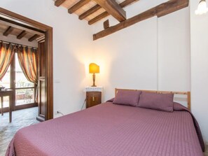 Une chambre à coucher avec une tête de lit en bois, un lit recouvert d’une couette rose, une lampe de chevet et une vue sur l’extérieur par une porte munie de rideaux.