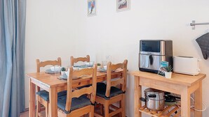 A dining area with a wooden table and chairs, a coffee machine, and a small kitchen setup with a pot and a toaster. - L'Enclave I et J by Interhome (Les Contamines)