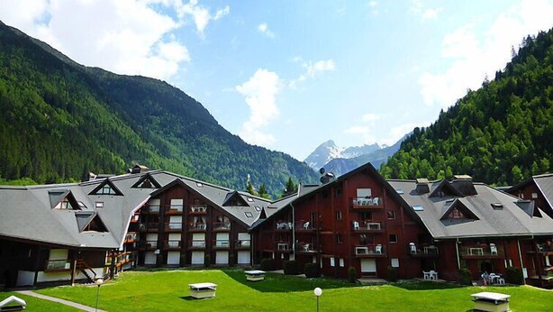 A cluster of chalet-style buildings with multiple balconies, set against a backdrop of lush green mountains and a clear sky. - L'Enclave I et J by Interhome (Les Contamines)