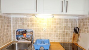 A kitchen with white cabinets, a stainless steel sink, a blue storage container, and a knife block. - L'Enclave I et J by Interhome (Les Contamines)