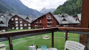 A balcony with a table set for two, a coffee pot, and two blue glasses. The view includes a row of wooden buildings with balconies and a mountainous landscape in the background. - L'Enclave I et J by Interhome (Les Contamines)