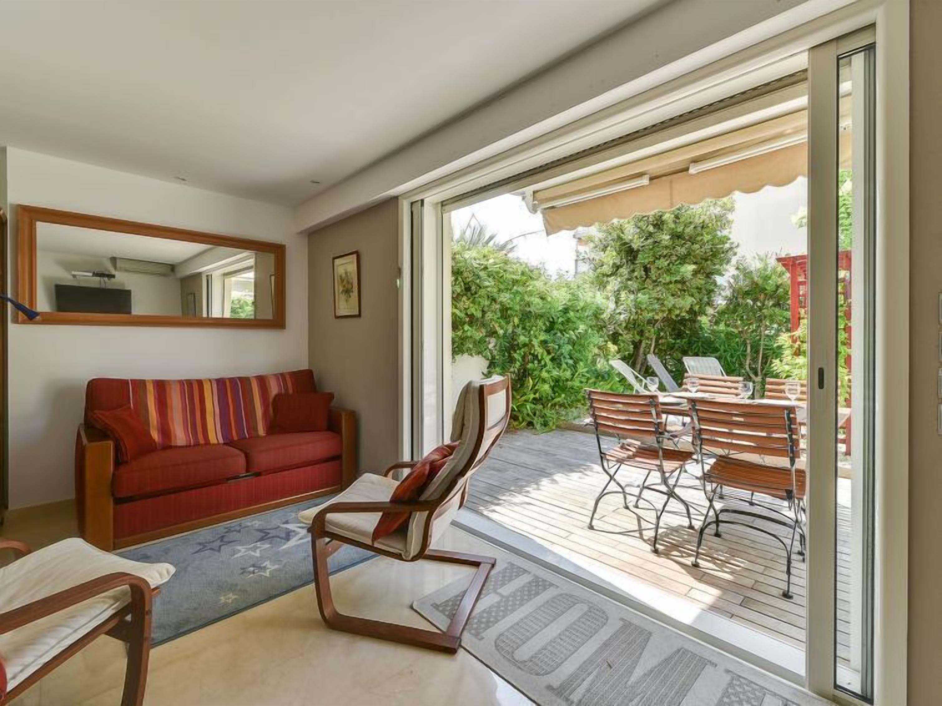 Una sala de estar con un sofá, una silla y una mesa de comedor con sillas. Hay una puerta corrediza de vidrio que da a un patio exterior con una mesa y sillas.