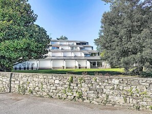 A modern multi-story building with a flat roof, large windows, and a stone wall in the foreground.