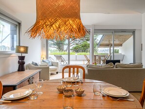 A dining area with a wooden table set for four, surrounded by a modern living space with a sofa and chairs.