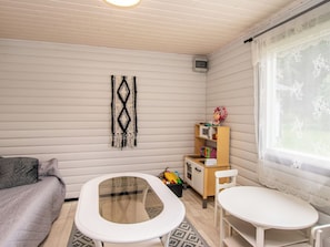 Une pièce comprenant un lit, une petite table, une chaise, un espace de jeu pour enfant et une fenêtre avec des rideaux en dentelle.