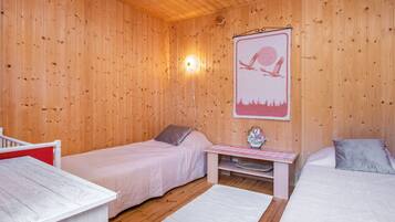 A wooden cabin room with two beds, a small table, and a wall-mounted light fixture.