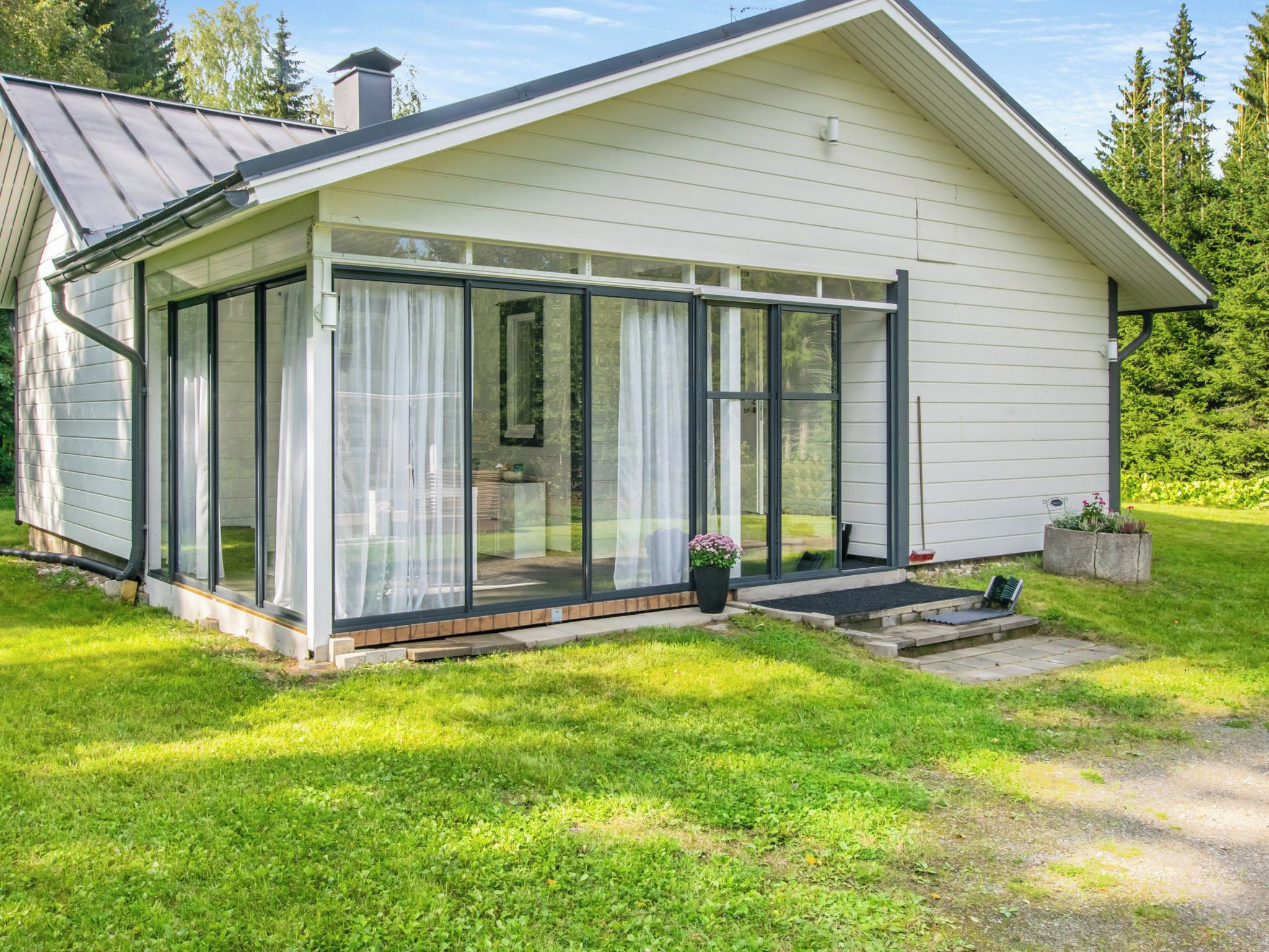 A modern house with a glass-enclosed porch, a chimney, and a well-maintained lawn.