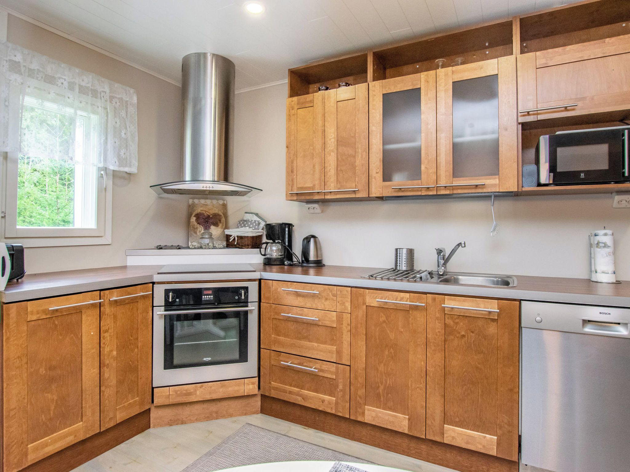 Een moderne keuken met houten kastjes, roestvrijstalen apparatuur en een raam met uitzicht op groen.