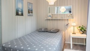 Une chambre à coucher avec un lit, une table de chevet, une lampe, un miroir et deux tableaux encadrés accrochés au mur.
