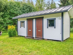 Een laag, rechthoekig gebouw met twee deuren en een raam, omringd door gras en bomen.