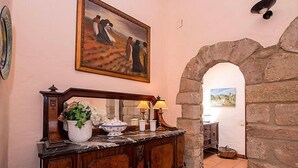 Un intérieur traditionnel avec une arche en pierre, une console en bois sur laquelle est posé un vase de fleurs, et un tableau accroché au-dessus.