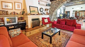 Un salon chaleureux avec une cheminée, des canapés rouges et une arche en pierre qui mène à une autre pièce.