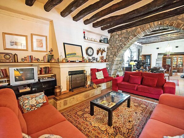Un salon chaleureux avec une cheminée, des canapés rouges et une arche en pierre qui mène à une autre pièce.
