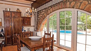 Un espace repas avec une grande table et des chaises en bois, une cheminée en pierre et une vue sur une piscine, visible à travers de grandes portes vitrées.