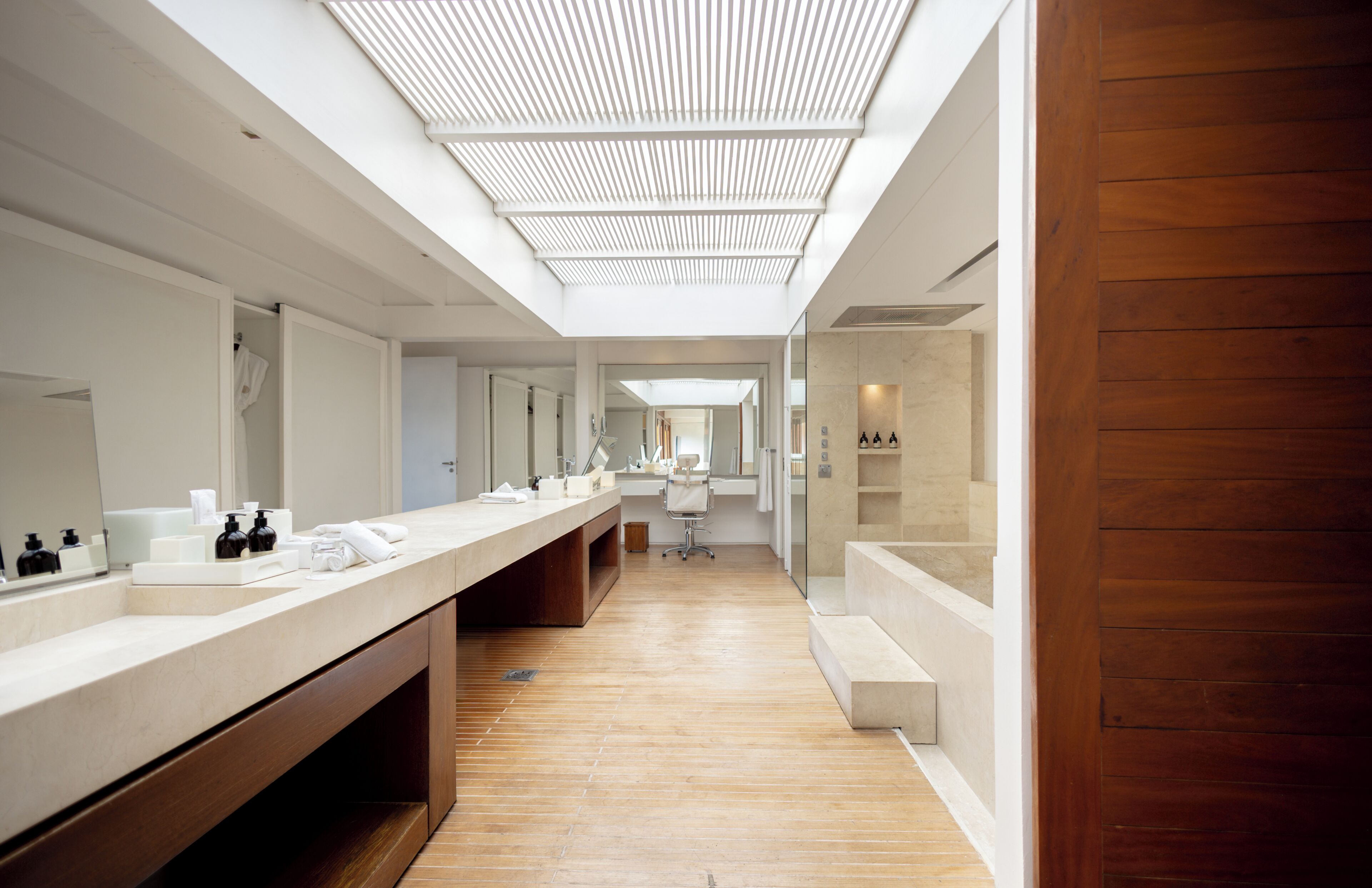 A modern bathroom with a long vanity, a skylight, and a wooden floor.