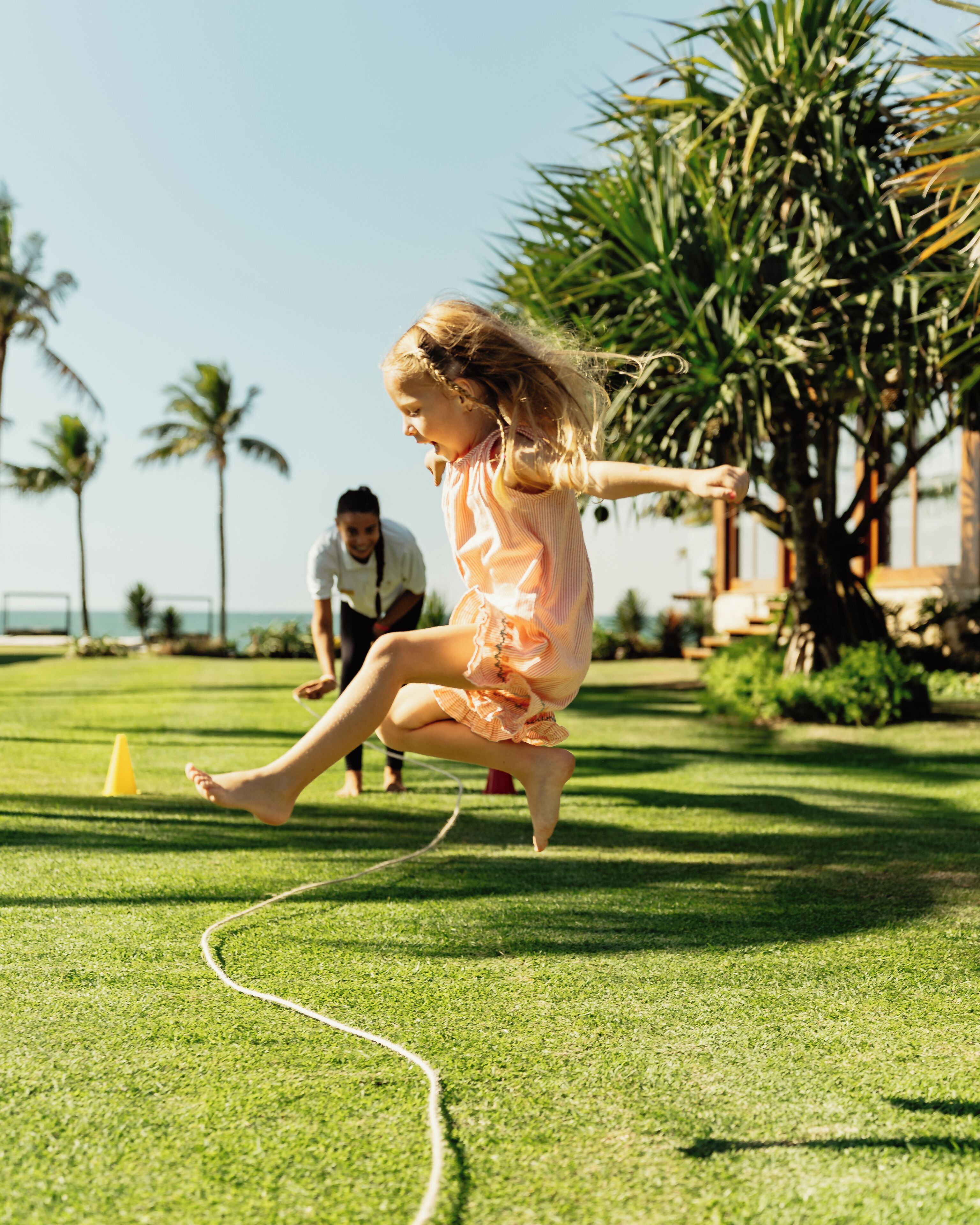 A grassy area with a person jumping and another person in the background.